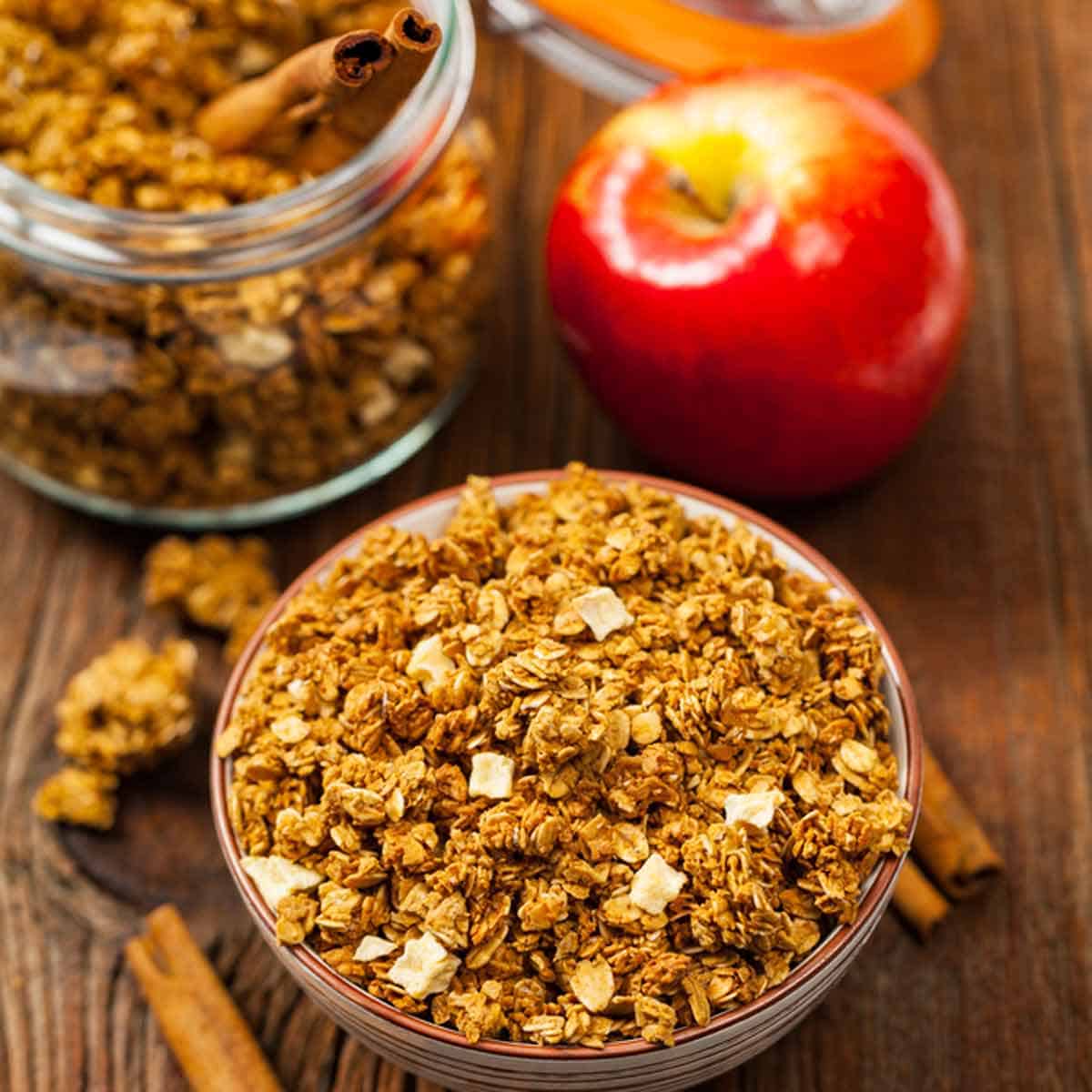 granola A bowl of apple granola with a fresh apple in the background.