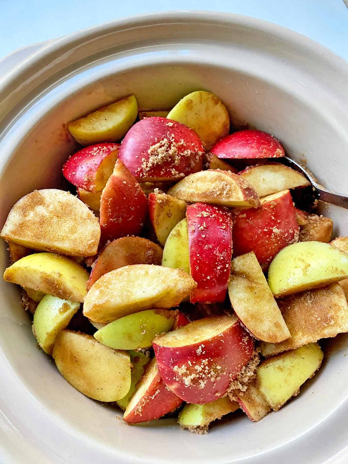 Cut up apples, brown sugar and spices in a slow cooker ready for cooking.