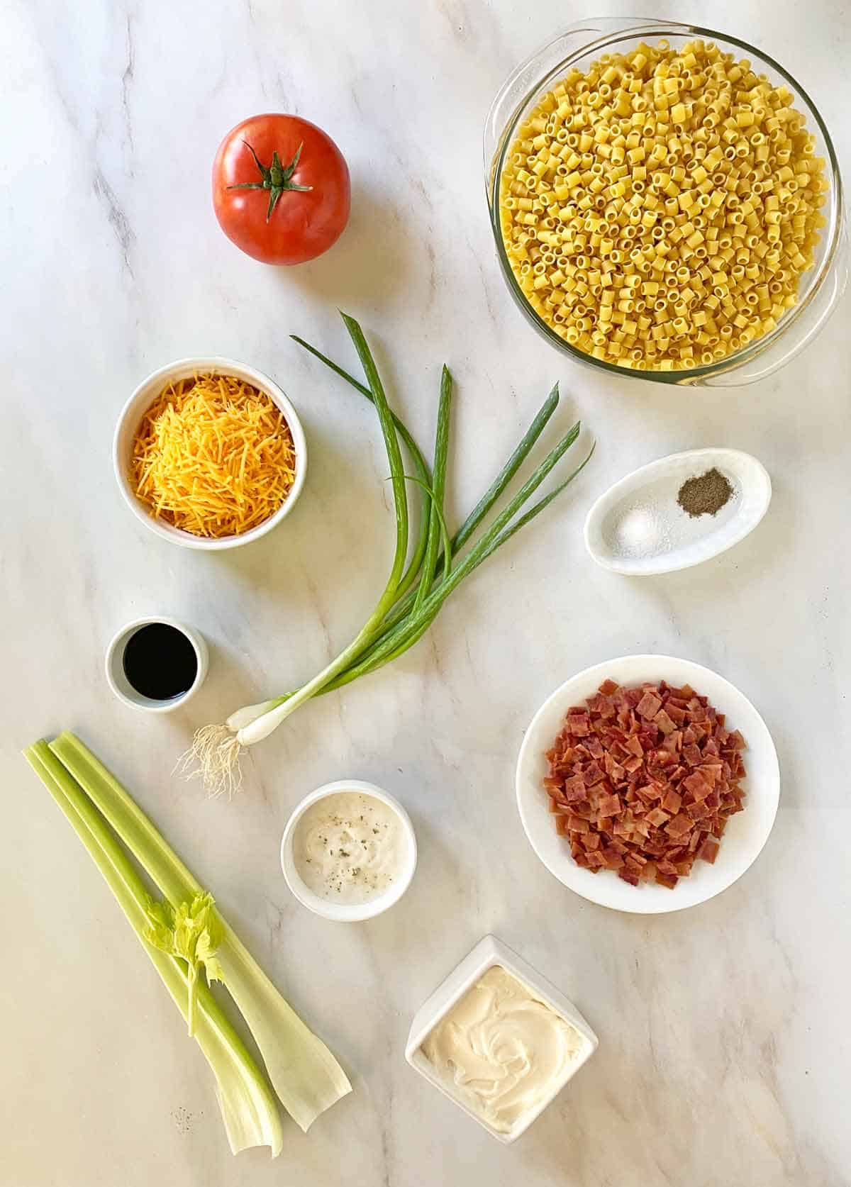 Macaroni, a tomato, shredded cheese, green onions, seasonings, dressing, celery, mayonnaise and cooked bacon.