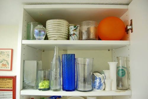 A crowded cabinet filled with 25 glass and ceramic vases.
