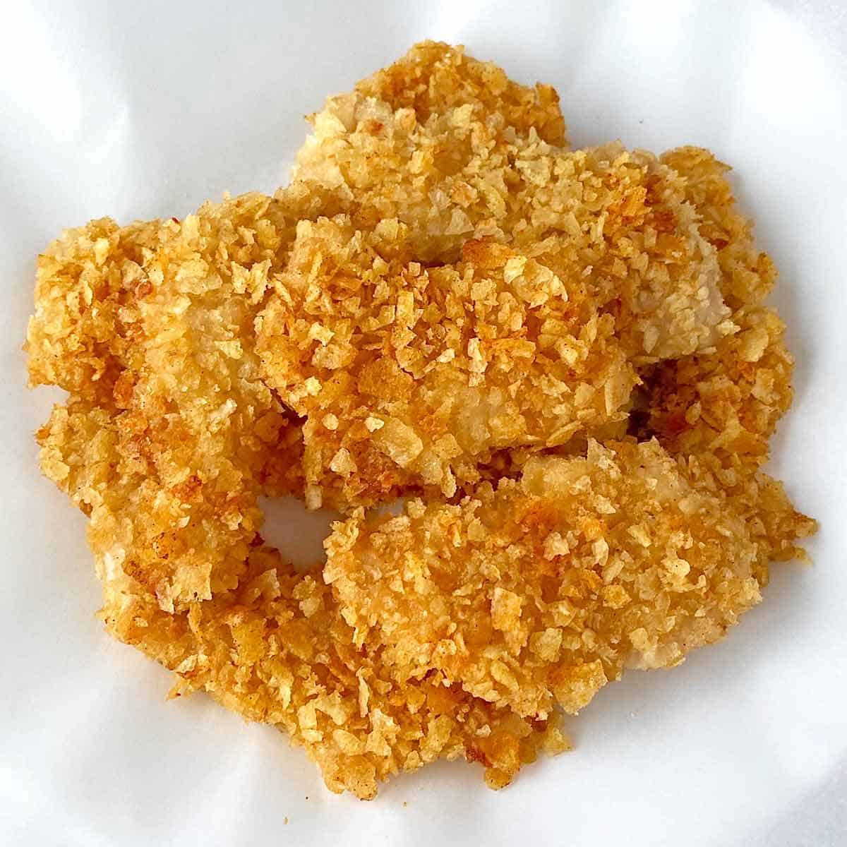 Crispy golden brown potato chip chicken nuggets piled on a piece of parchment paper.