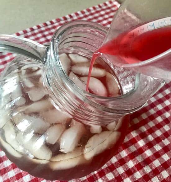 Pouring the red currant juice into the honey iced tea mixture in a pitcher.