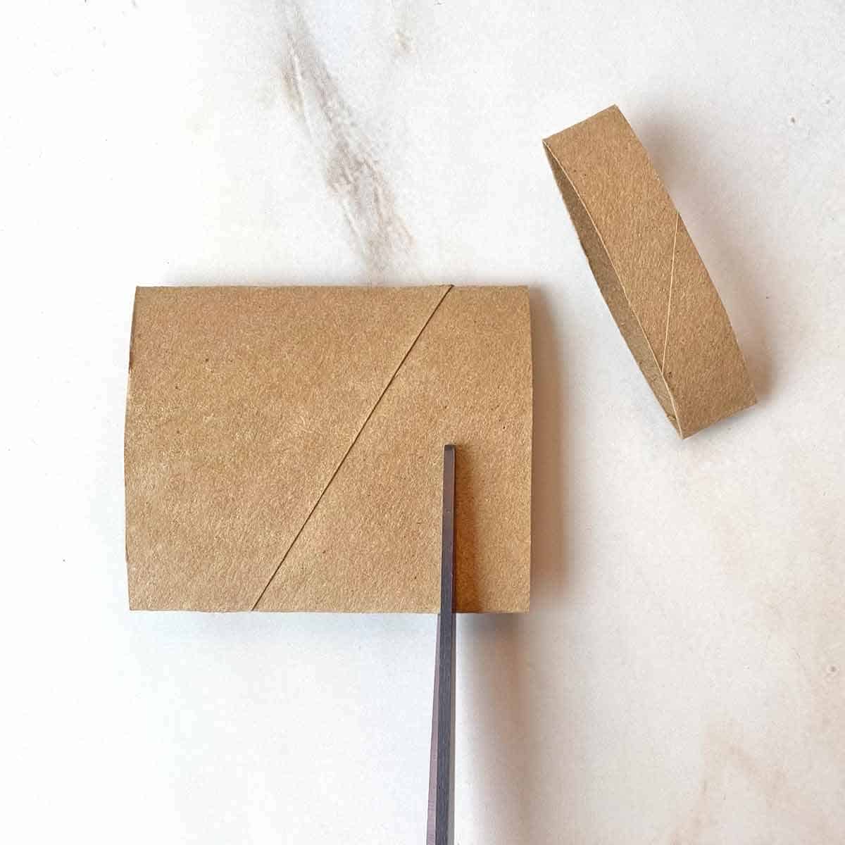 Cutting a flattened toilet paper tube into sections for crafting.