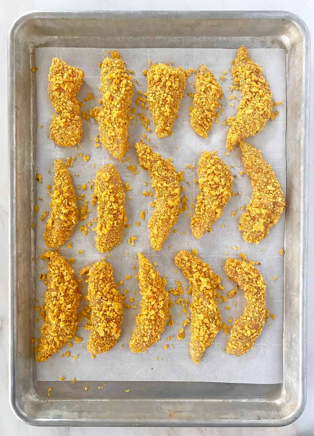Overhead shot of cool ranch chicken tenders on a baking sheet before being baked.