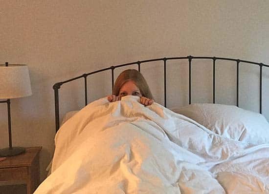 Eliza Cross hiding under the covers in bed.