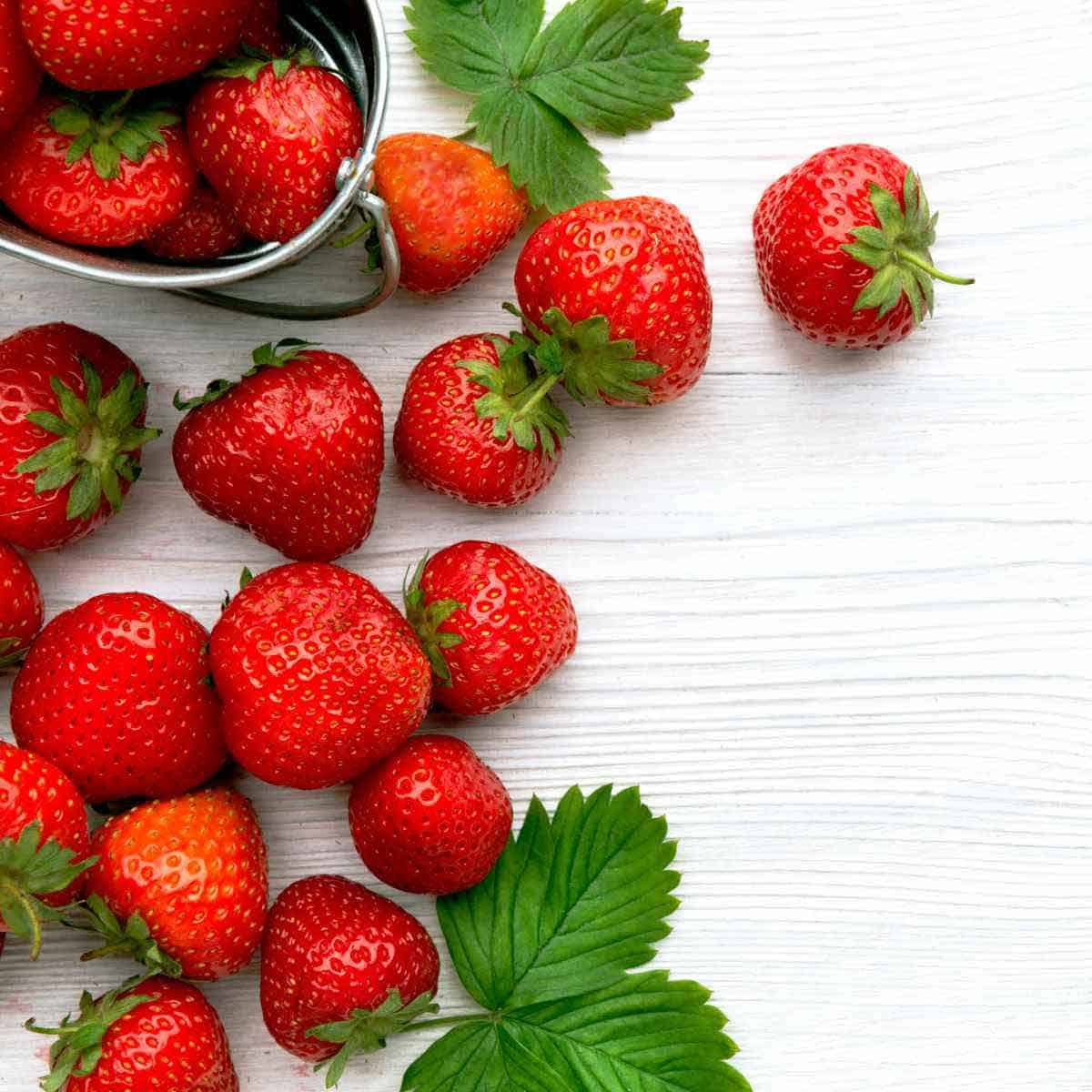 A quart of fresh strawberries on a white board.
