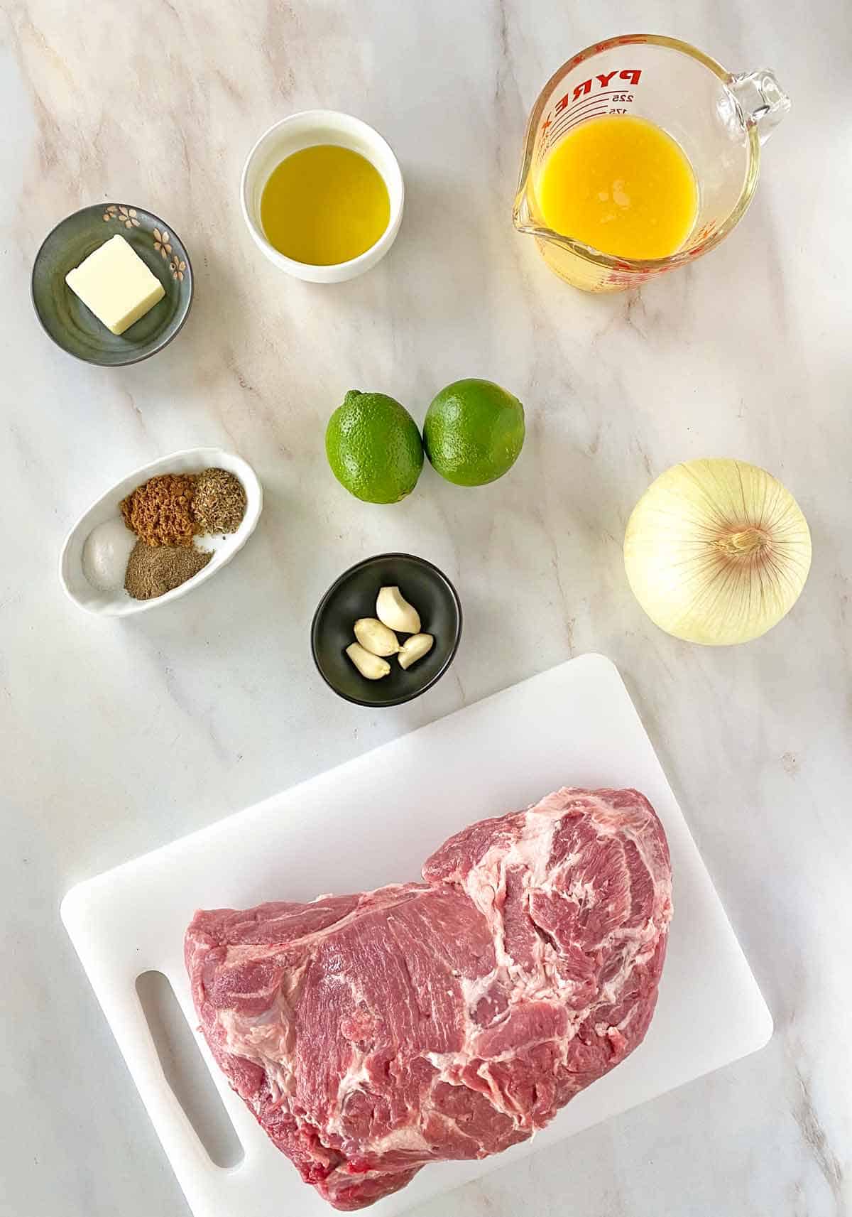 Orange juice, olive oil, limes, onion, garlic, spices, pork shoulder and seasonings to make Mexican Carnitas in the slow cooker.