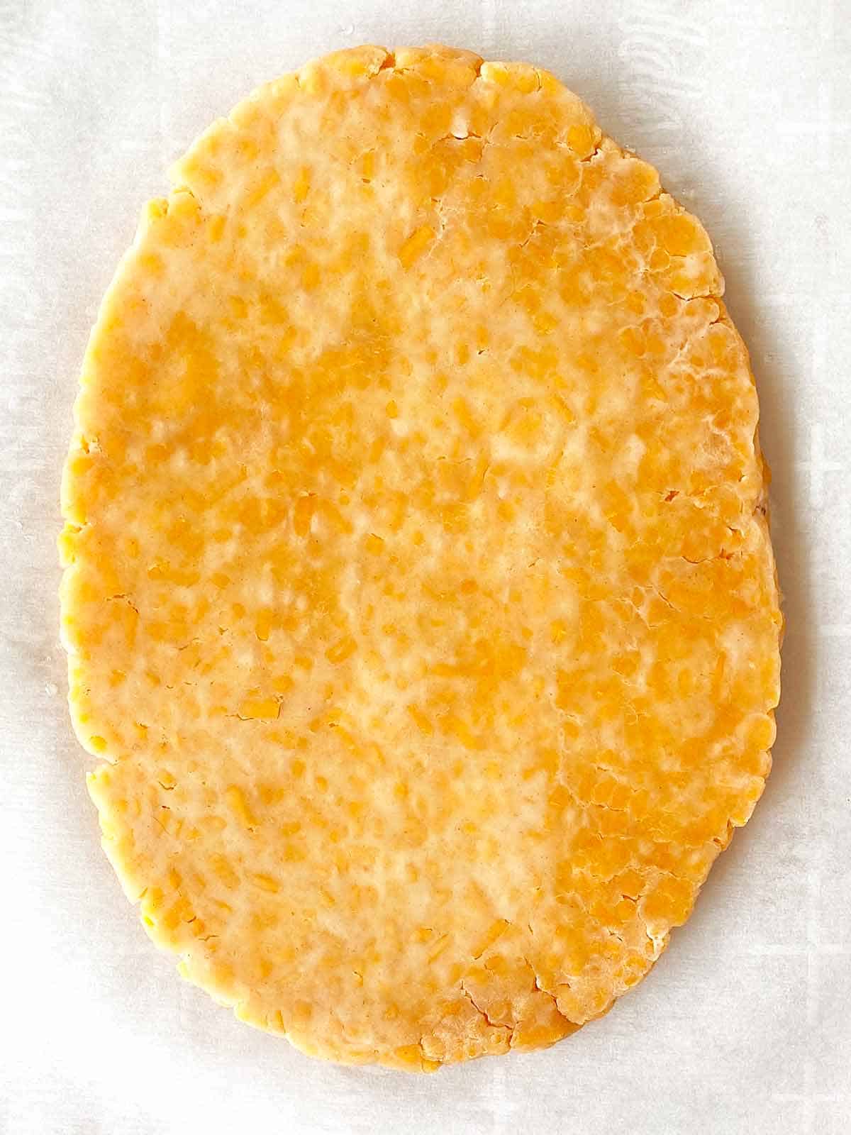 Crackers8 An oval of partially rolled cheez cracker dough on parchment paper.