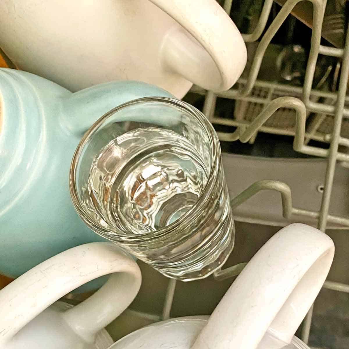 A small shot glass filled with homemade rinse aid in a dishwasher.