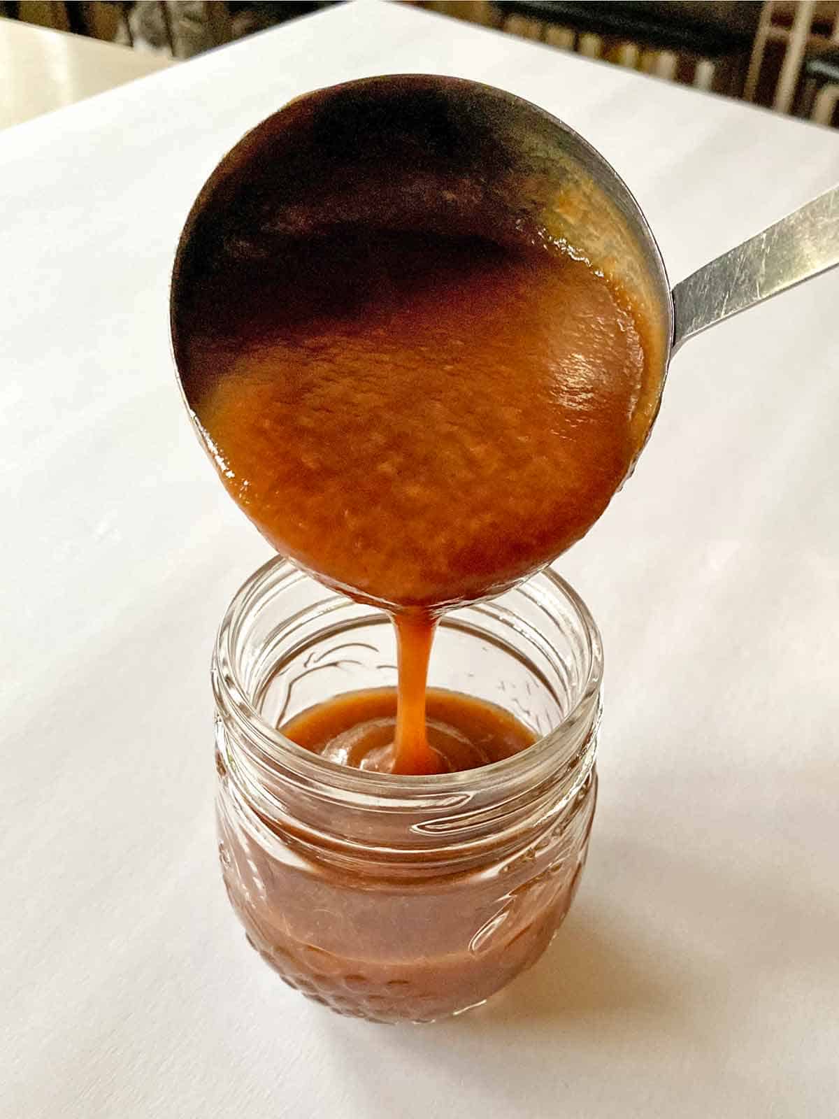 Using a ladle to pour hot cooked apple butter into a sterilized jar.