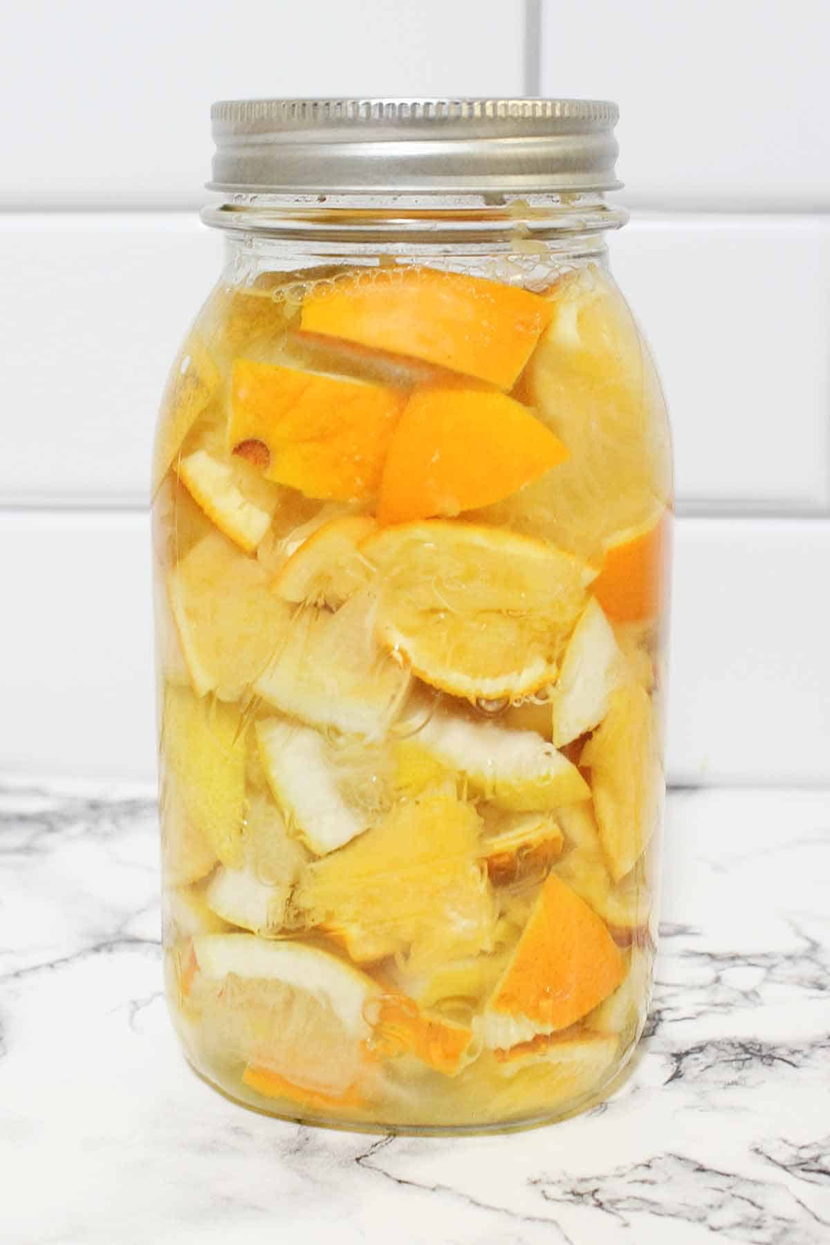 Lemon and orange peels steeping in vinegar in a glass Mason jar.