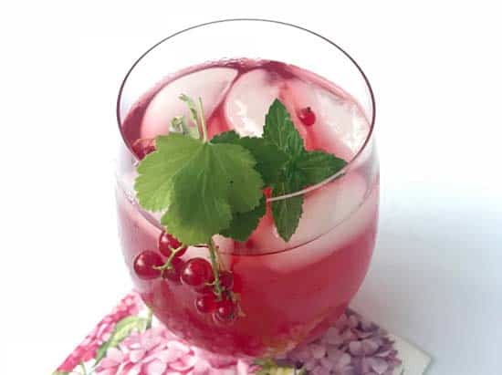 Finished glass of red currant honey iced tea garnished with fresh currants and currant leaves.