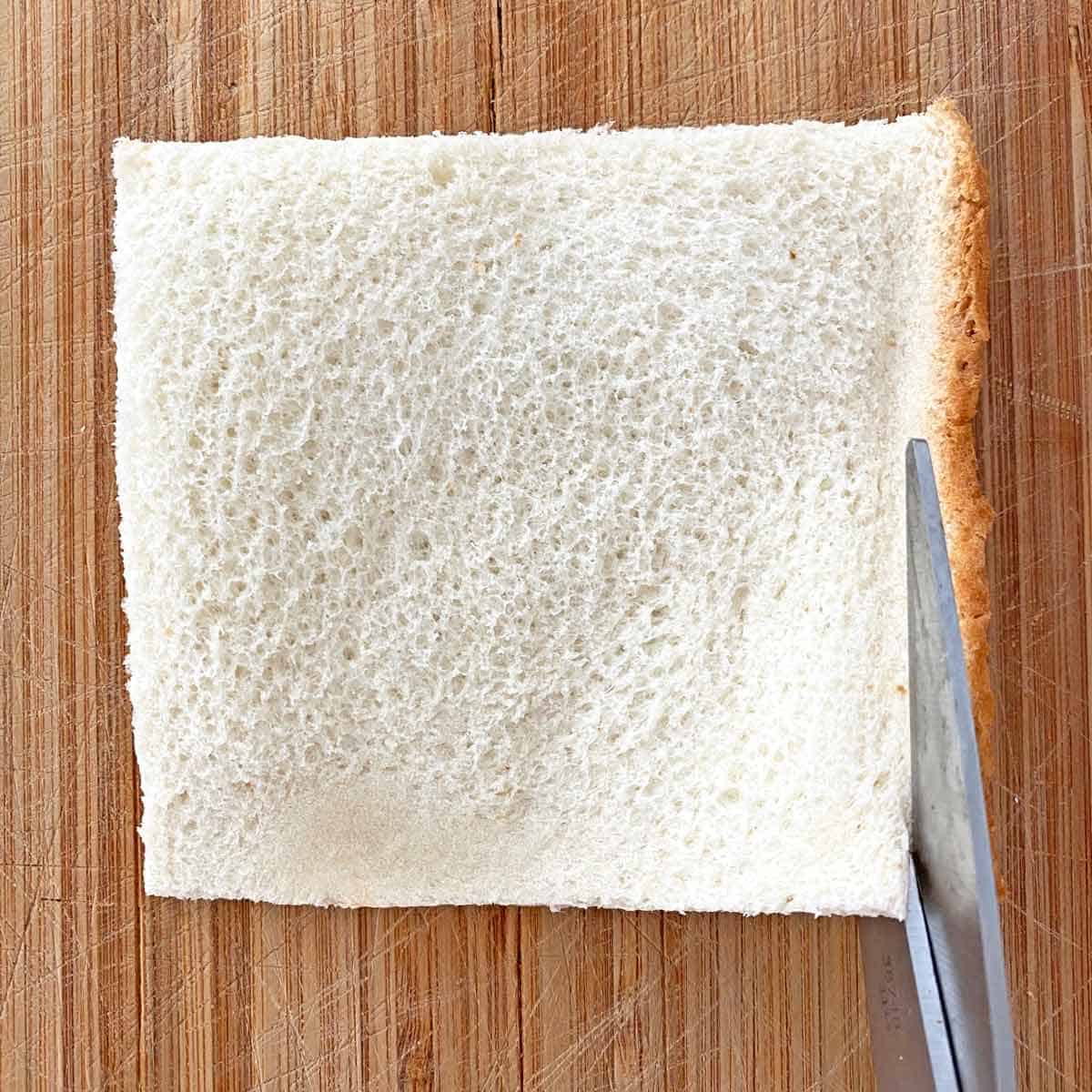 Cutting crusts off a flattened piece of bread with kitchen scissors.