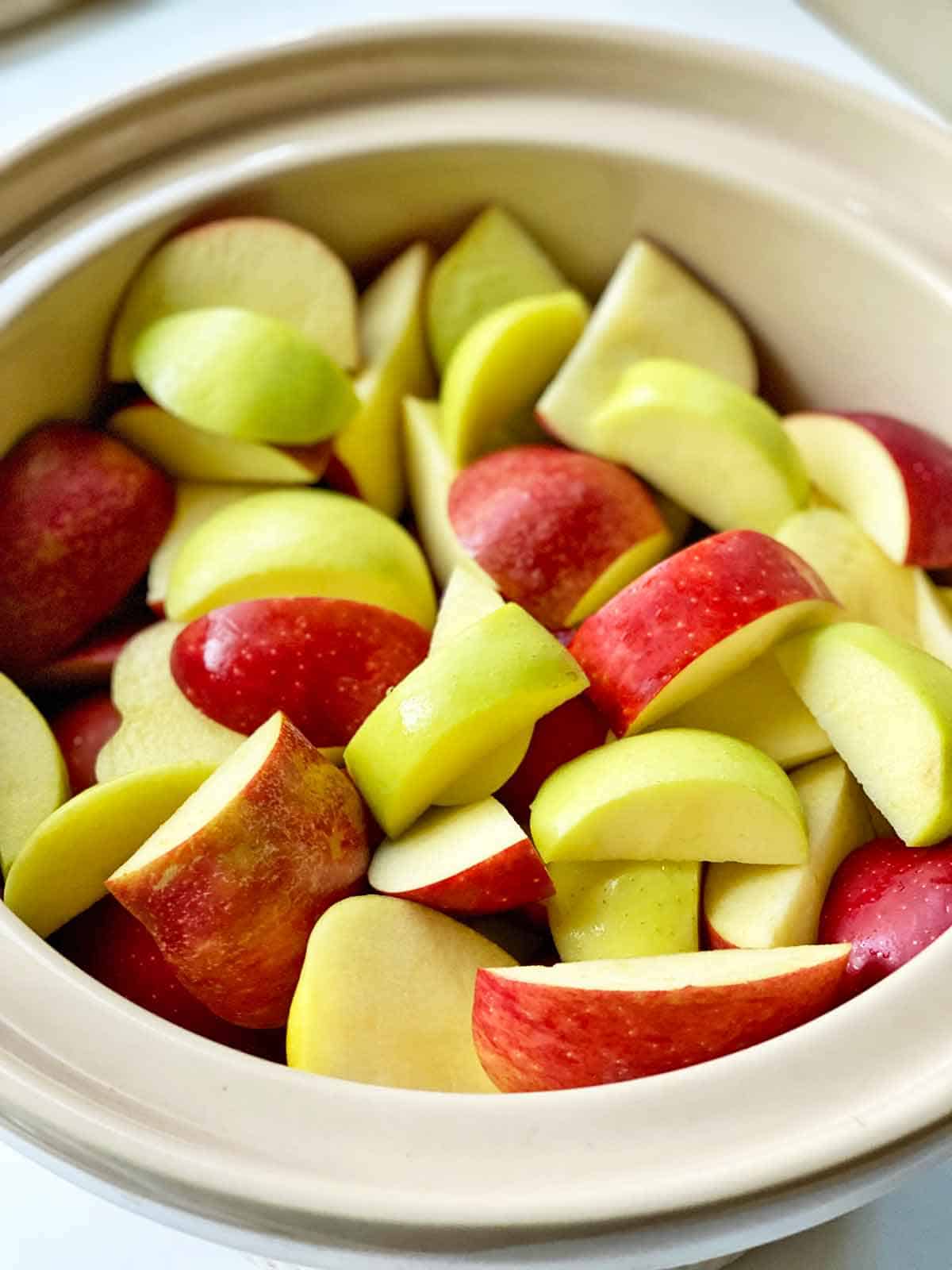 Red and green apple slices in the liner of a slow cooker.